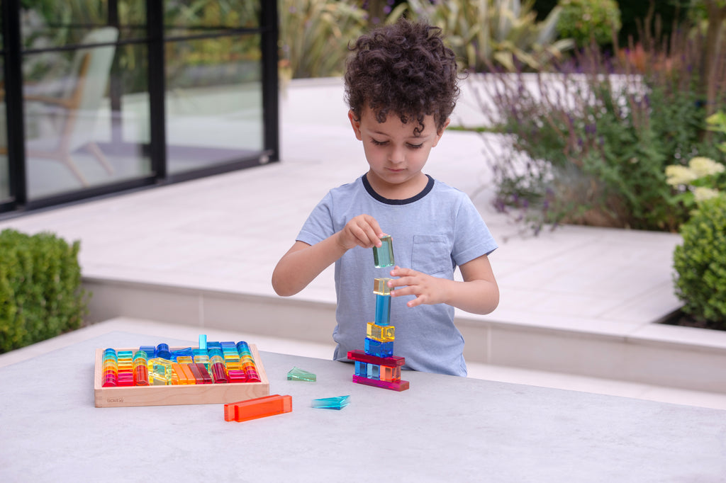 Child plays with colorful gem building shapes tray and transparent block structures