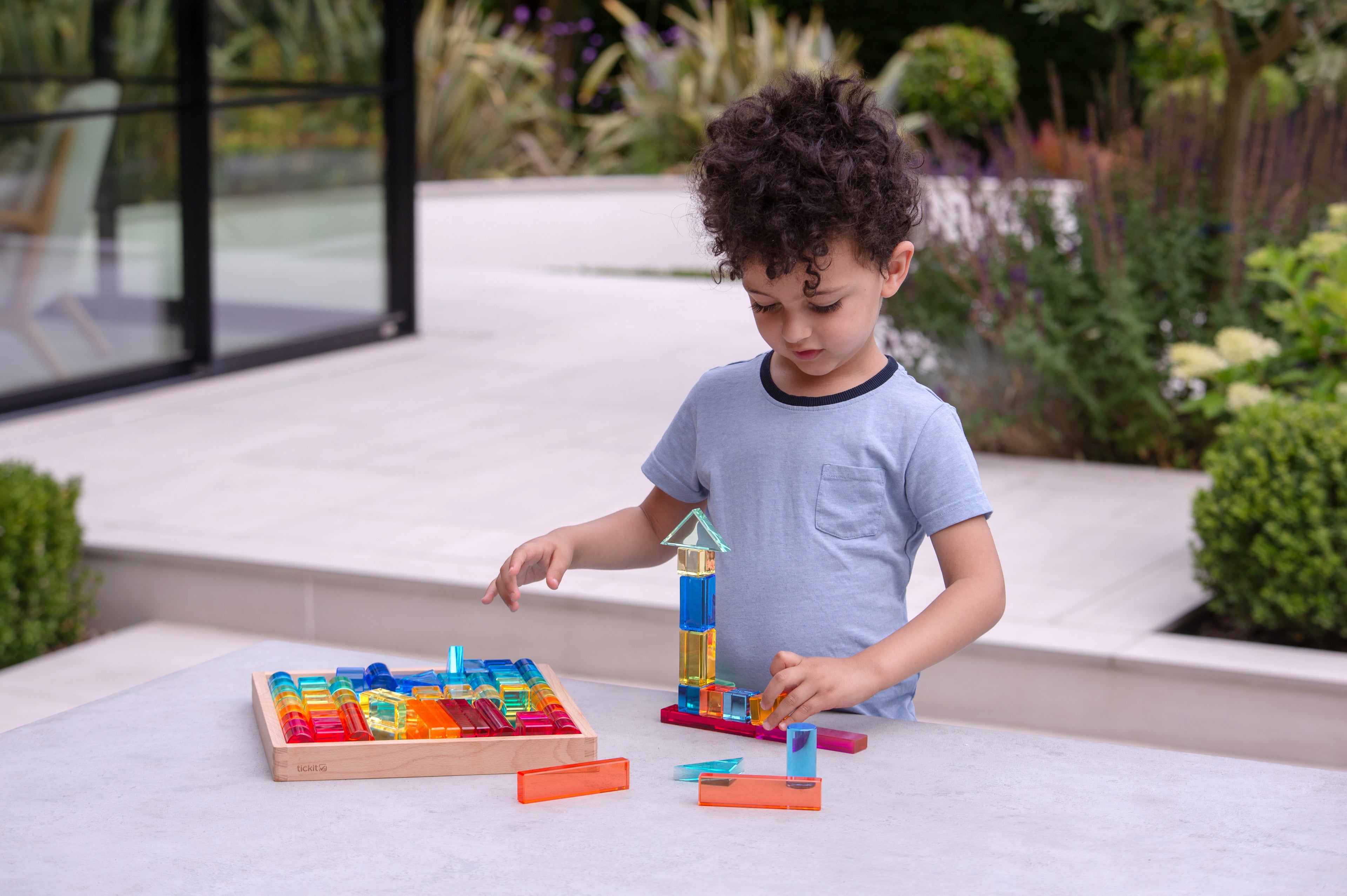 Child builds with transparent blocks beside a wooden gem building shapes tray
