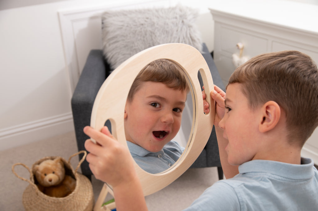 Light wood handheld round mirror with oval reflective glass, used by a child in front