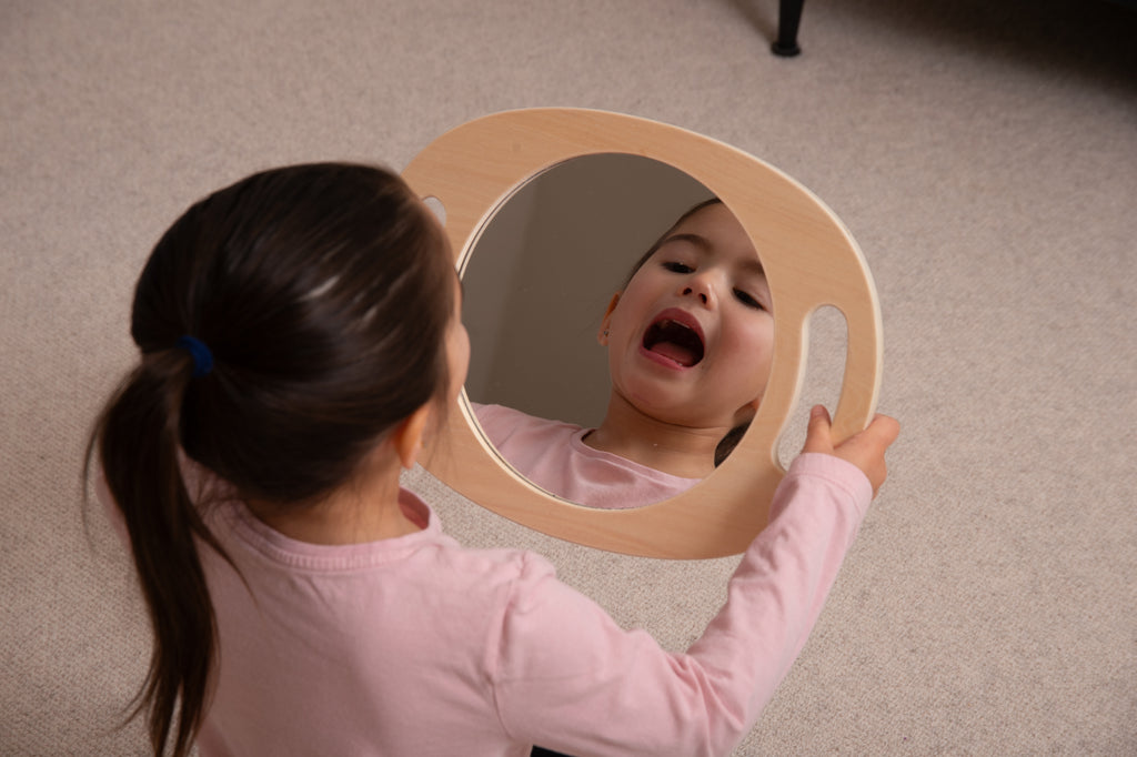 Light wood handheld round mirror with oval glass, held by a child from overhead