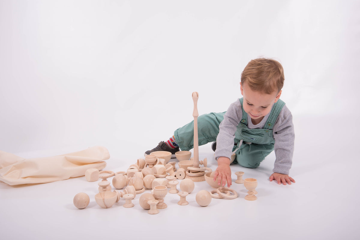 Wooden heuristic play starter set with rings and stackers; toddler reaches for a handle