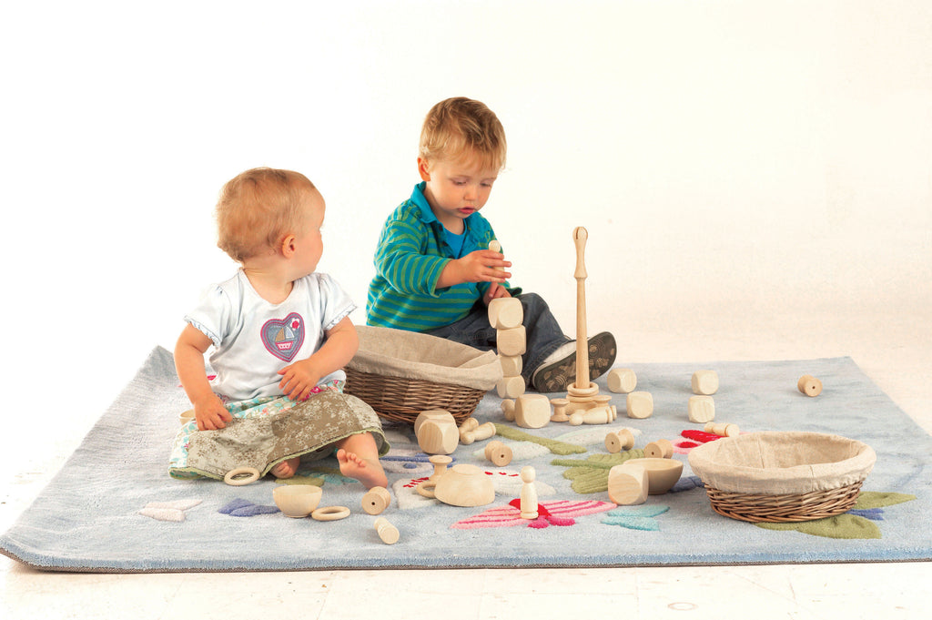 Wooden heuristic play starter set with stacking pieces, rings, and a basket on a mat