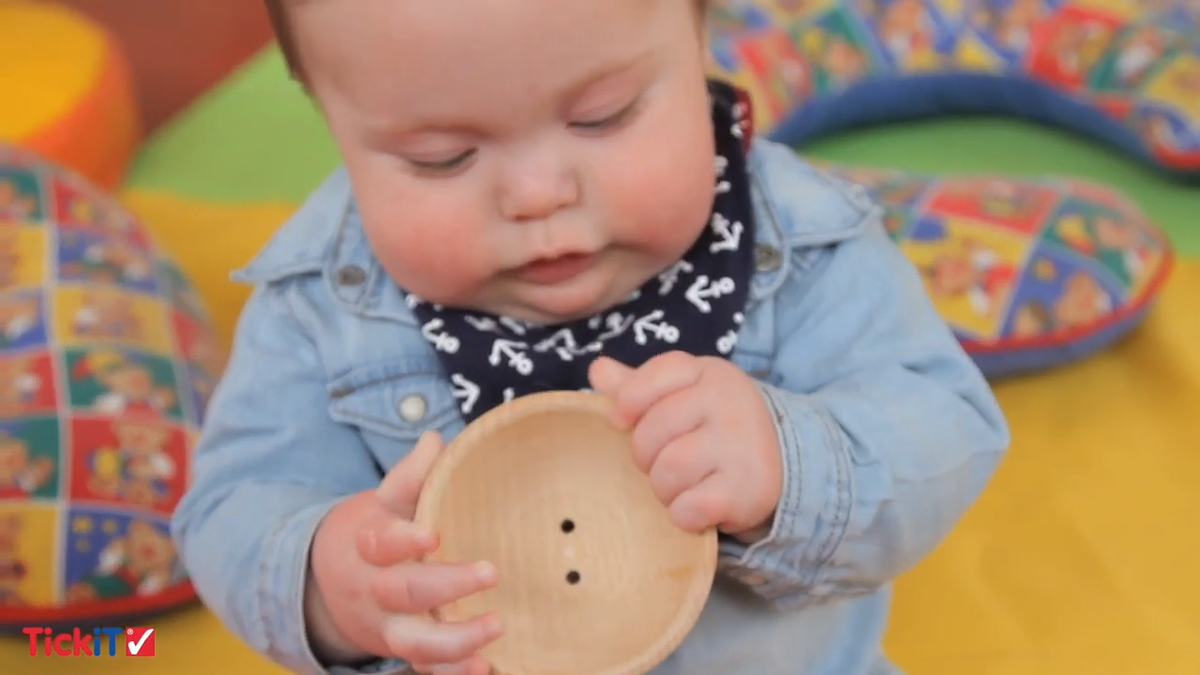 Baby holding round wooden board with holes; includes wooden stackers and rings