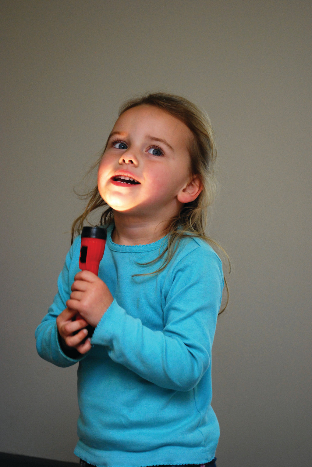Handheld LED torch, red body with bright white light, held by child