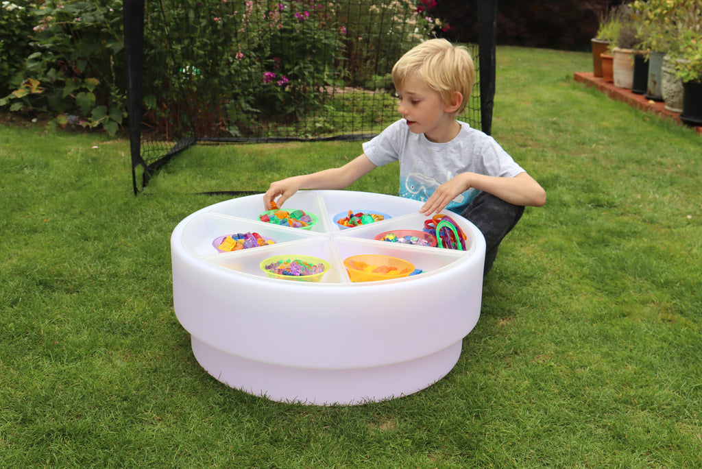 Round white bead sorting bowl on grass with multicolor compartments