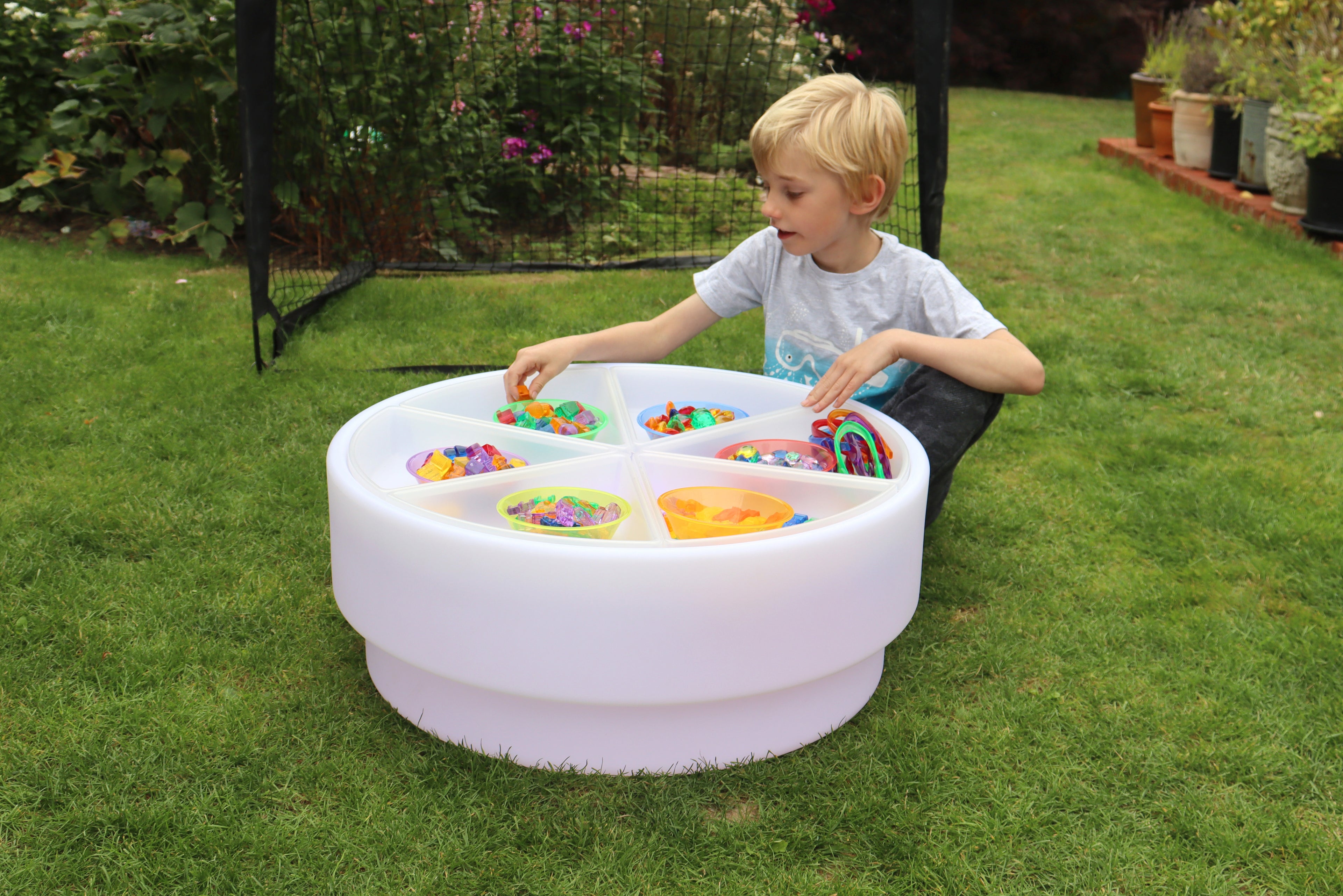 Round white bead sorting bowl on grass with multicolor compartments
