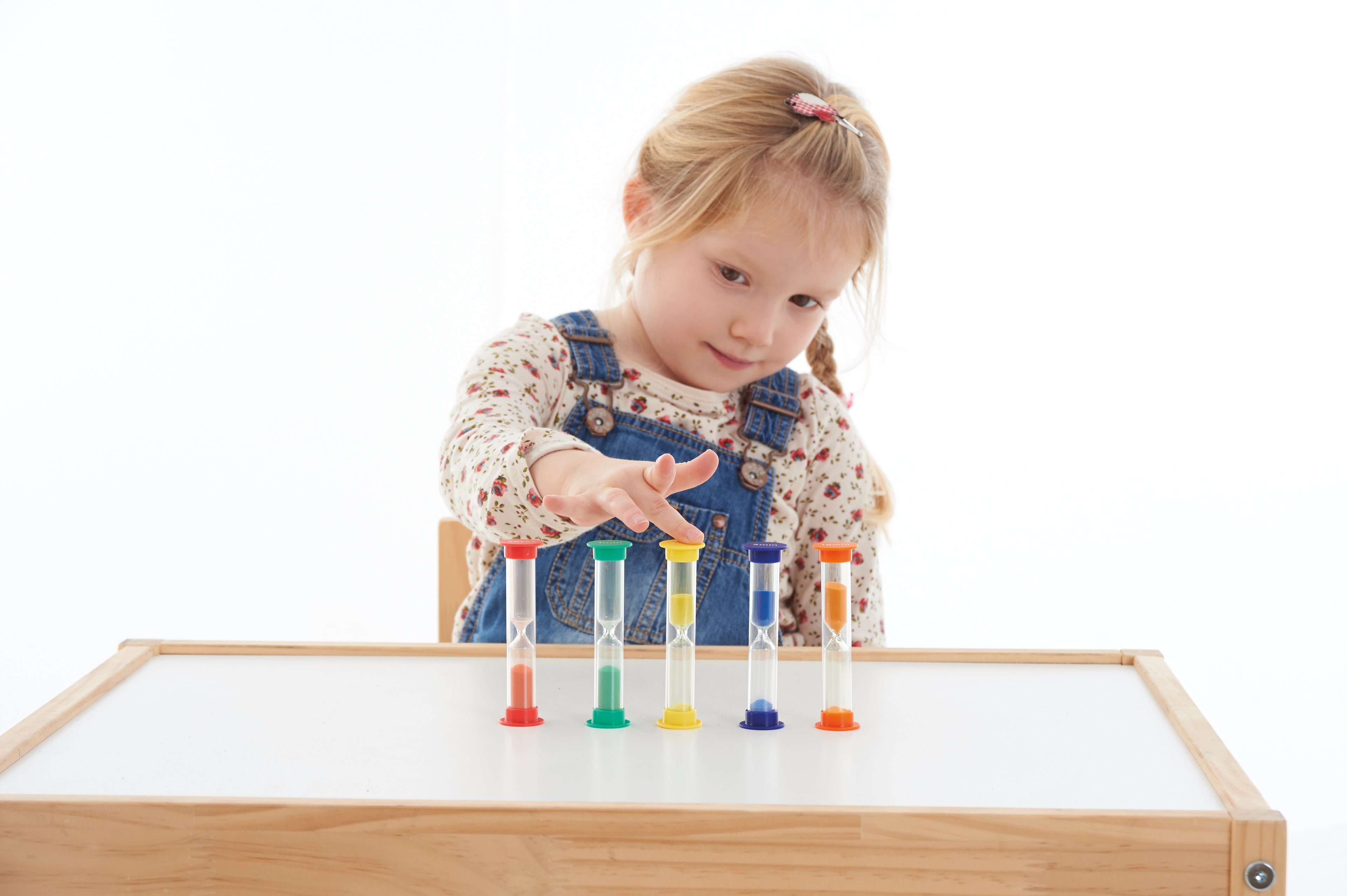 Mini sand timer set of five with colored caps and clear tubes on tabletop, child reaching