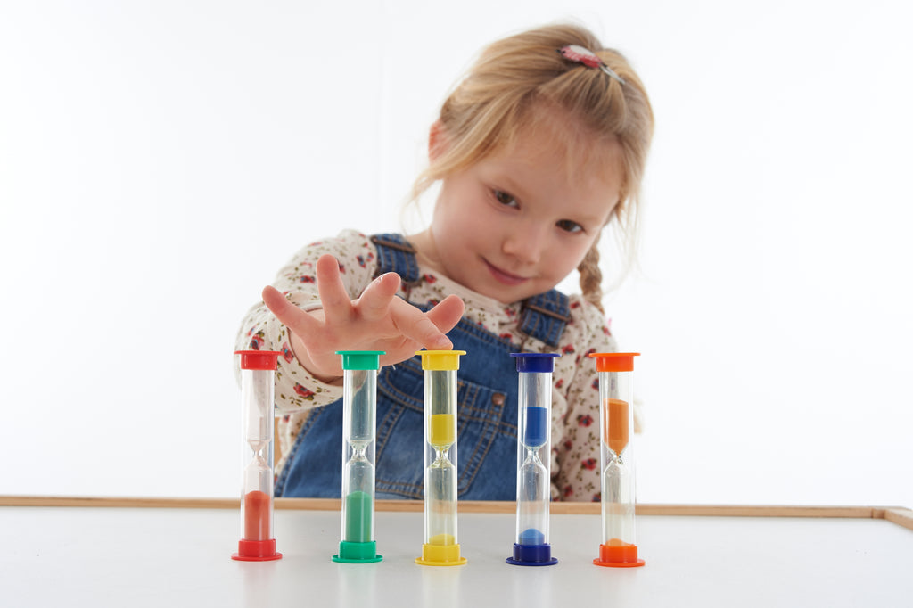 Five mini sand timers in different colors with clear tubes on table, child playing