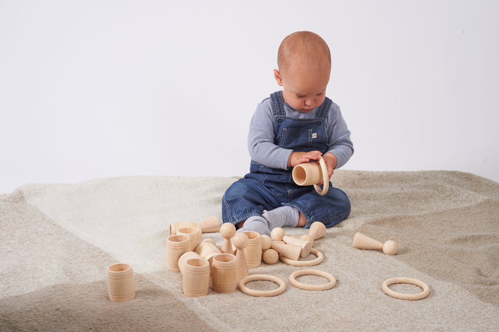 Natural wooden barrel toy with stacking rings, toddler holding it while playing