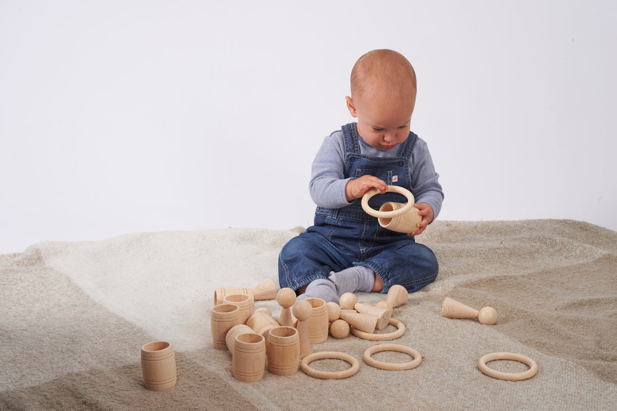 Natural wooden barrel toys and loop rings, toddler holding a ring