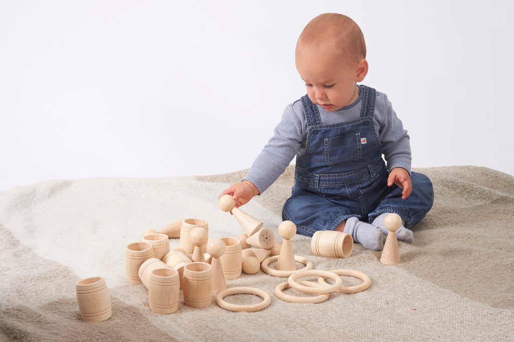 Natural wooden peg figures and ring pieces scattered on a light fabric play mat