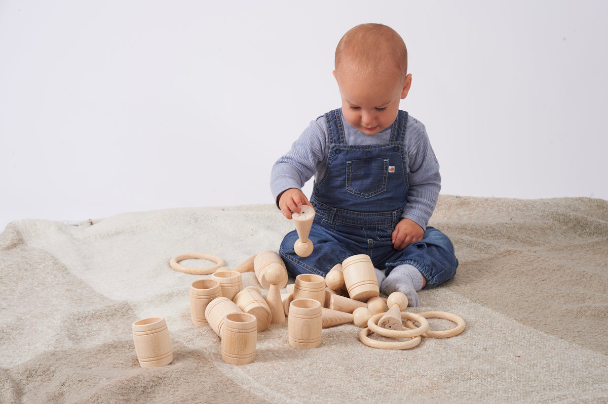 Natural wooden peg figures and loose wooden rings and cups on a fabric play mat