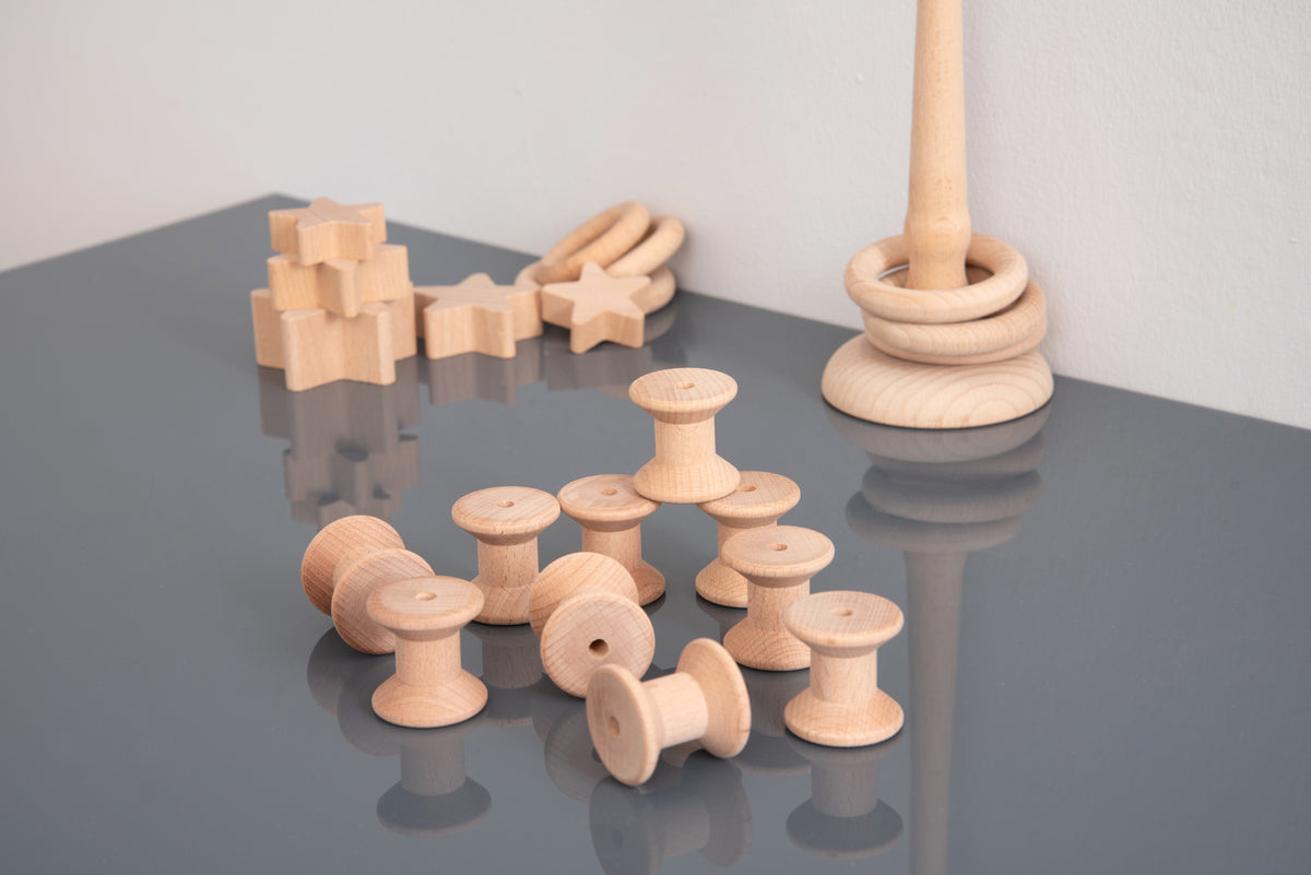 Natural wooden thread spool set beside a tall spindle stack of spools.