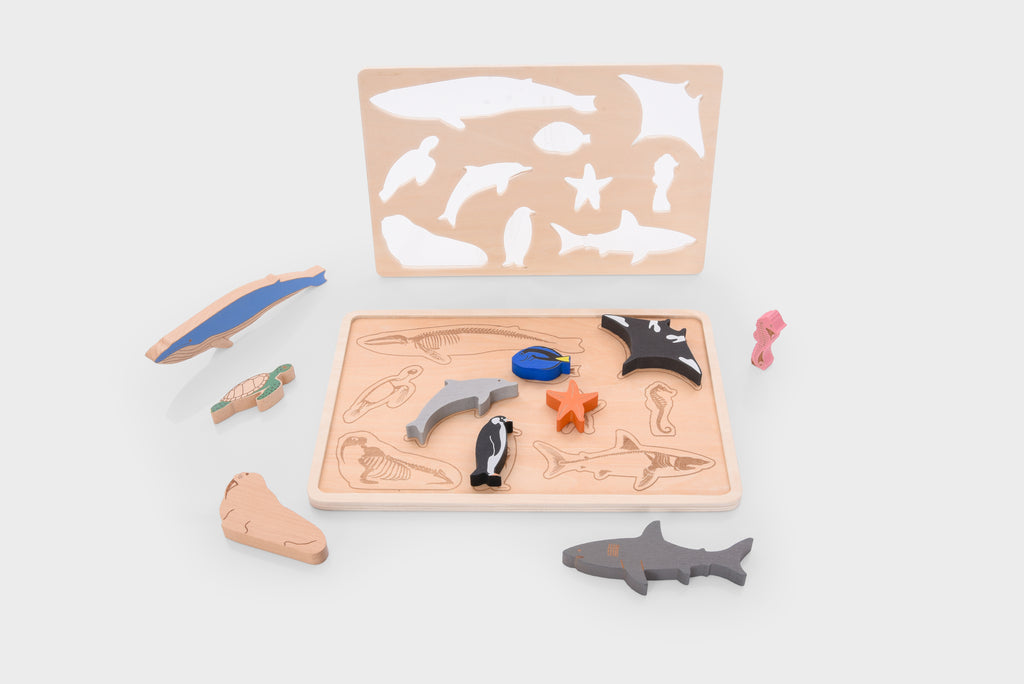 Ocean animal layer puzzle set with wooden base and cutout sea animals in blue, black, pink, and orange.
