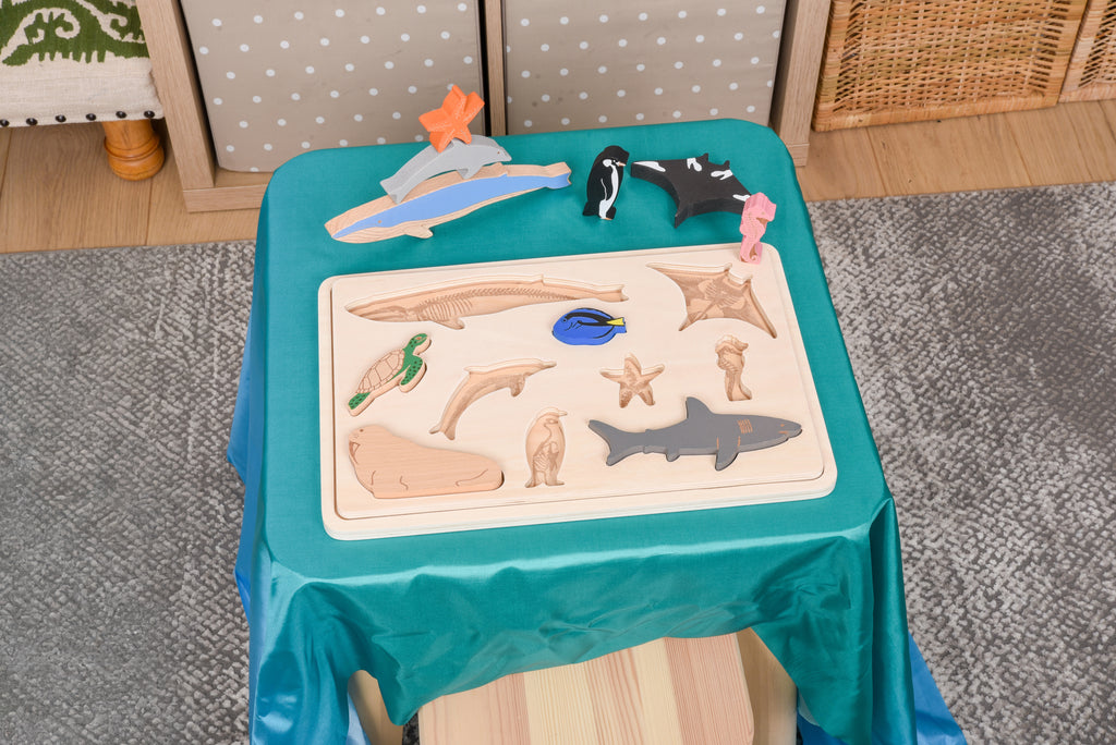Child-sized ocean animal layer puzzle on teal cloth table with wooden tray and layered ocean animal pieces.