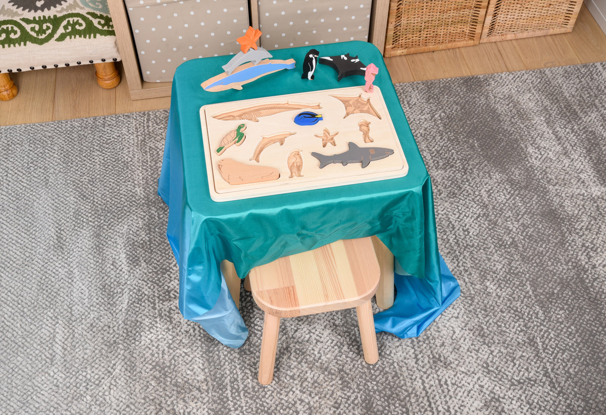 Ocean animal layer puzzle on a teal table with wooden base and sea animal cutouts, plus a chair nearby.