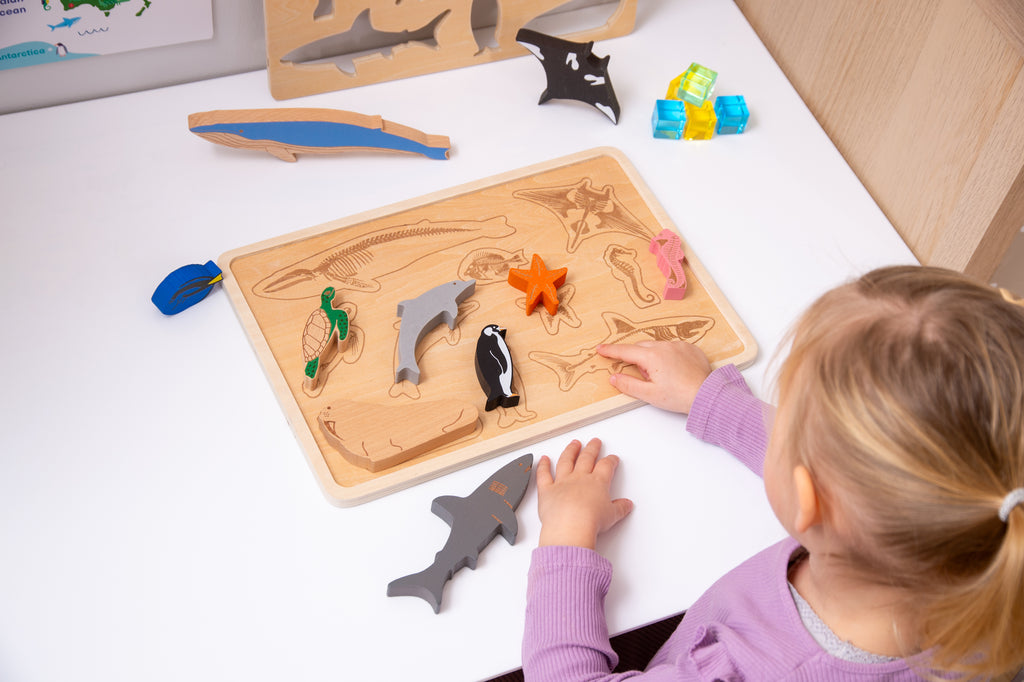Child playing with ocean animal layer puzzle trays, arranging shark and fish pieces on the wooden base.