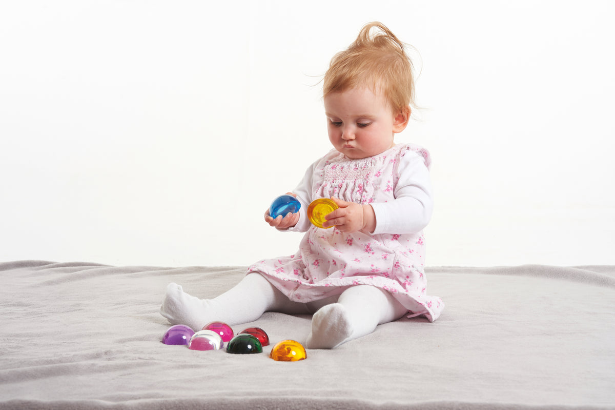 Toddler holding a blue hemisphere with other colorful hemispheres on blanket