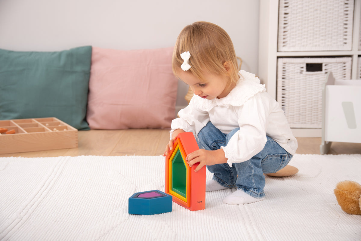 Toddler kneeling with rainbow nesting house blocks and small base pieces
