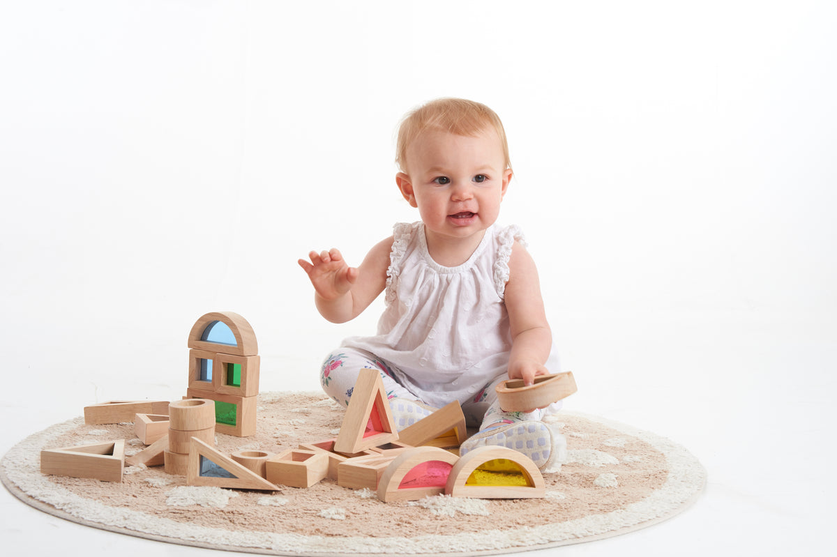Wooden rainbow block set on round play mat with stacked shape blocks