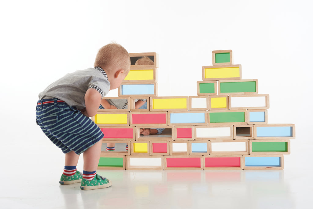 Toddler standing beside wooden rainbow window bricks stacked into a wall