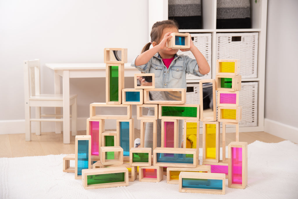 Kid playing with wooden rainbow window bricks stacked into a house-like tower