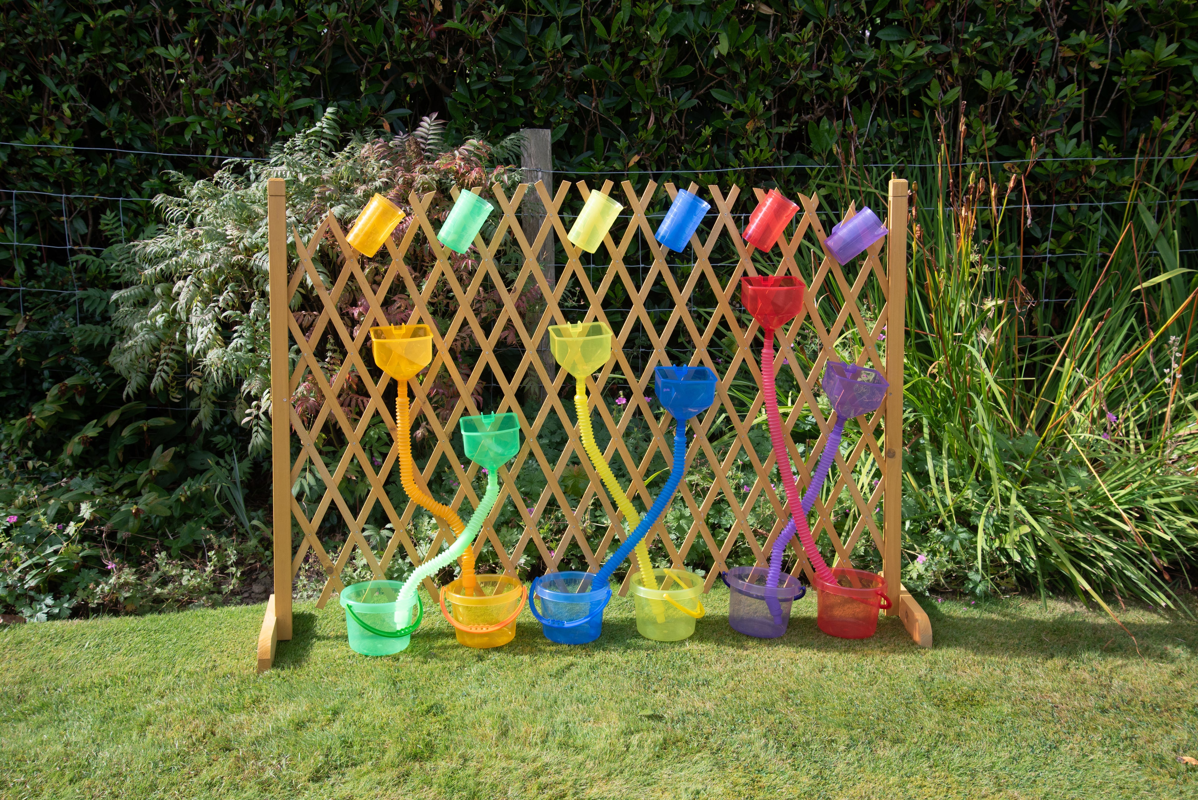 Outdoor display of rainbow flexible tube sprayers and scoop cups on a wooden panel