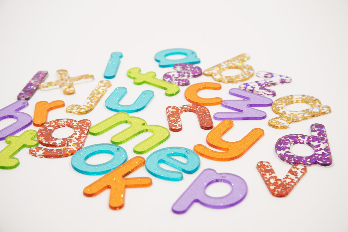 Colorful glitter alphabet letter cutouts scattered and overlapping on a white background