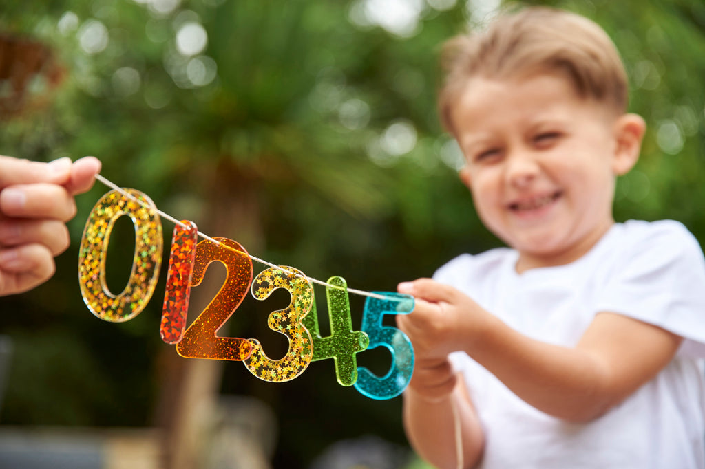 Rainbow glitter number banner with colorful digits 0 2 3 4 5 held by a smiling child