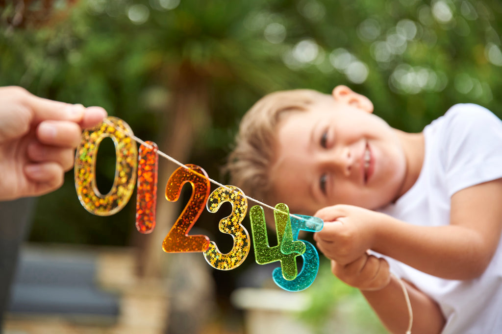 Rainbow glitter number banner with colorful digits 0 2 3 4 5 held by a child