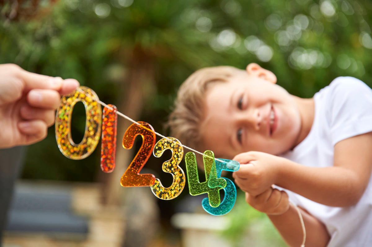 Rainbow glitter number banner with colorful digits 0 2 3 4 5 held by a child