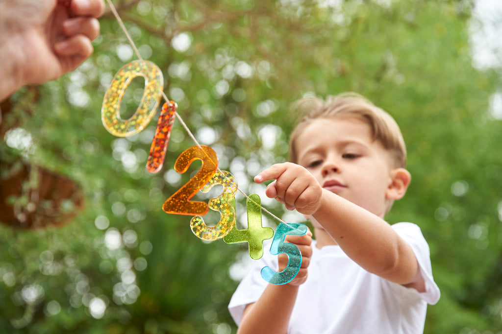 Rainbow glitter number banner with colorful digits 0 1 2 3 4 5 held outdoors
