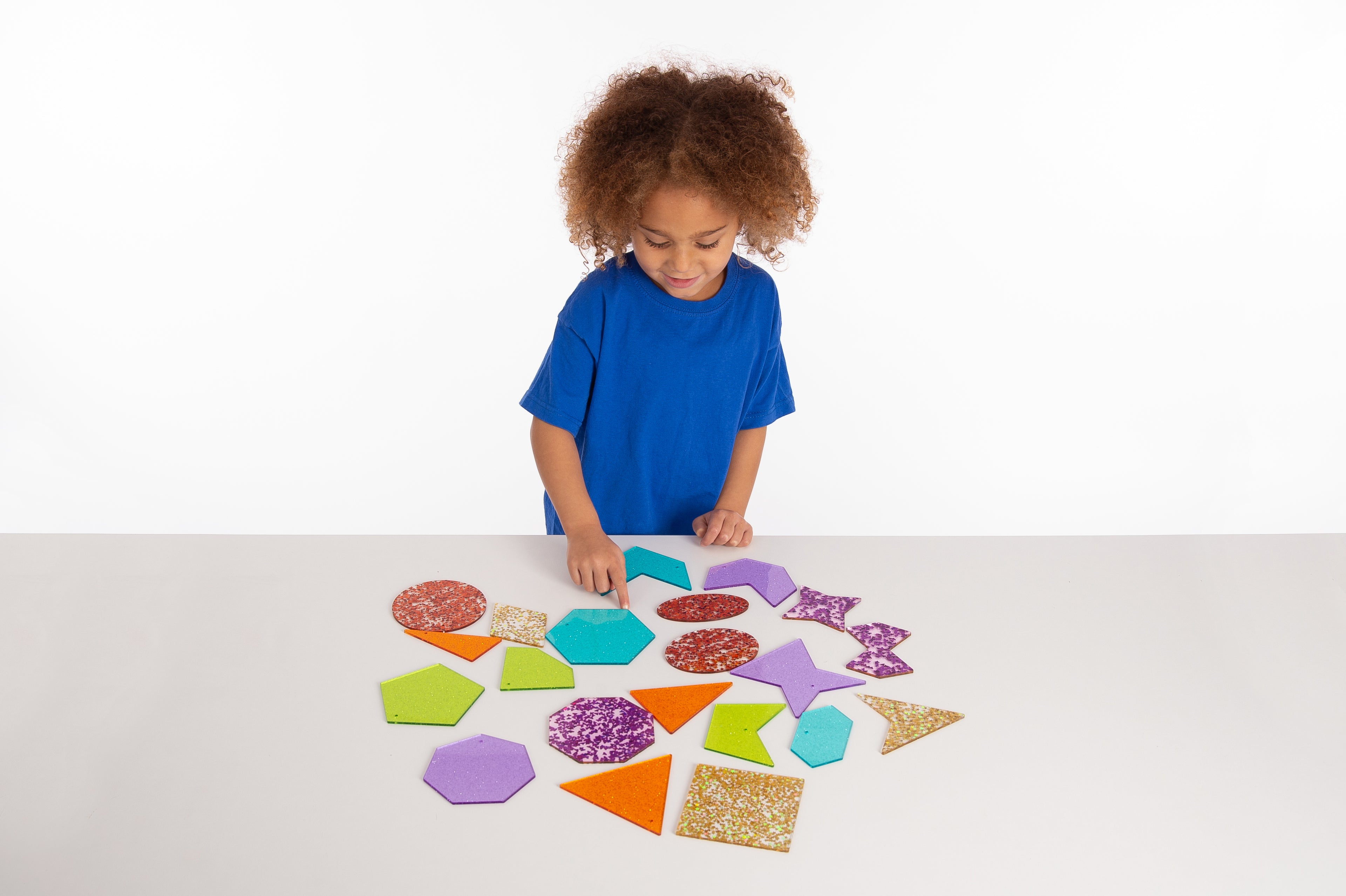 Child arranging colorful glitter shapes on tabletop, including stars and triangles