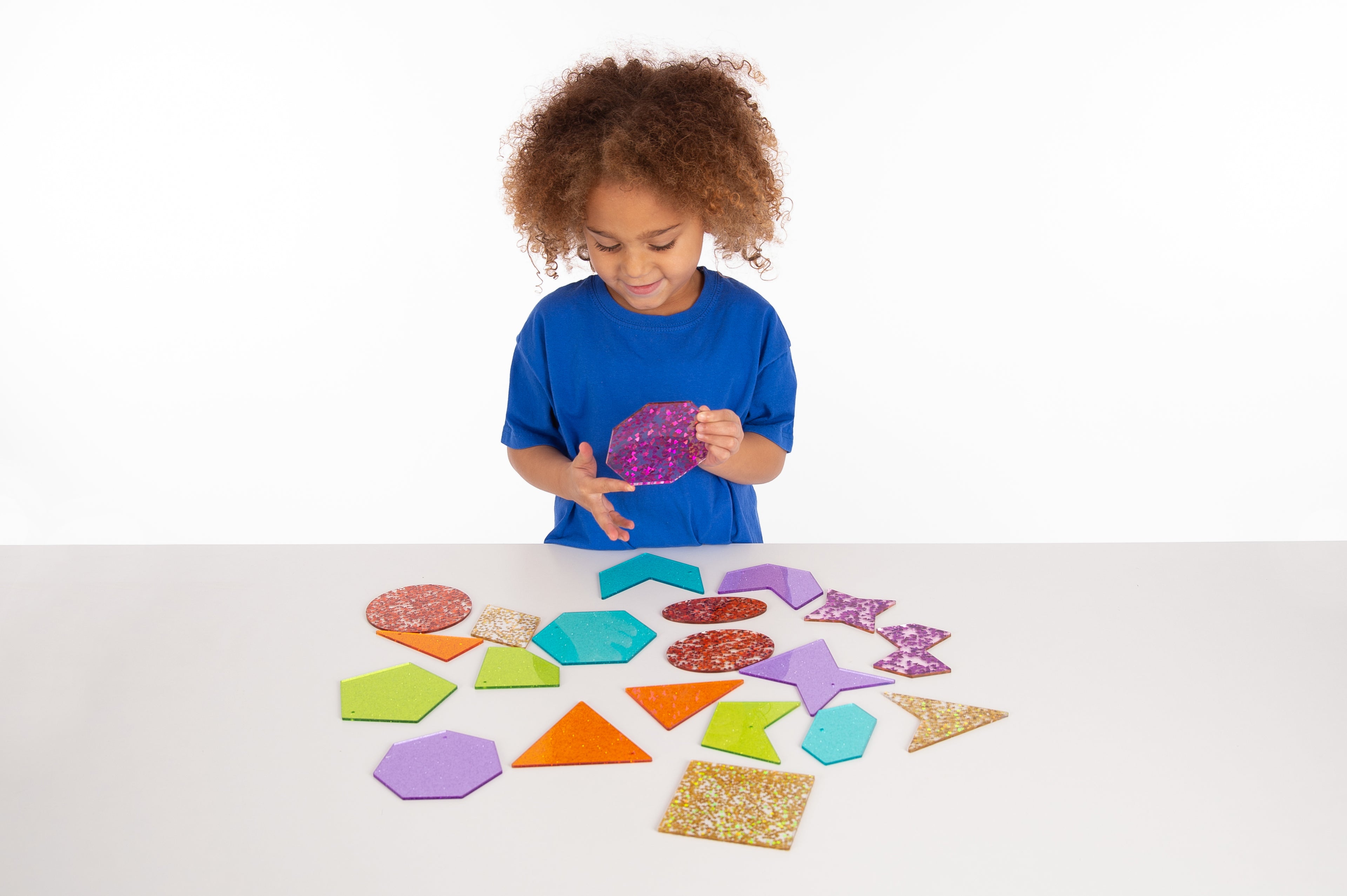 Child holding a purple glitter shape; colorful glitter foam shapes scattered on a table
