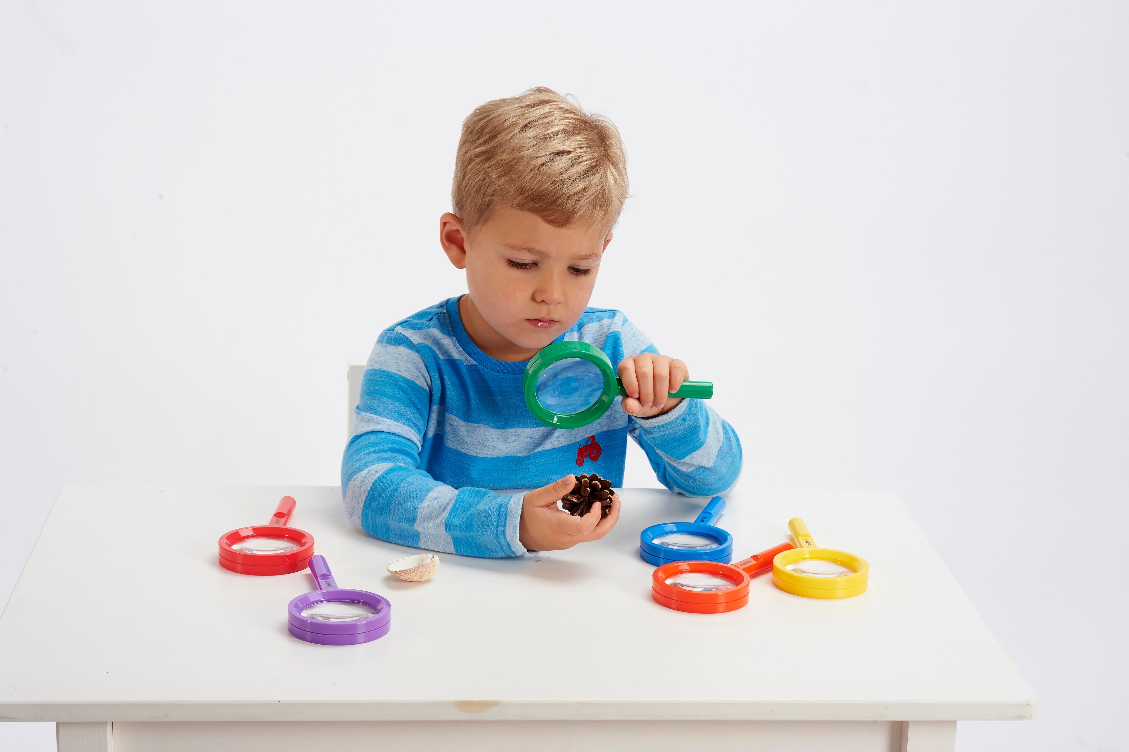 Child holding a green magnifying glass over toys on a table