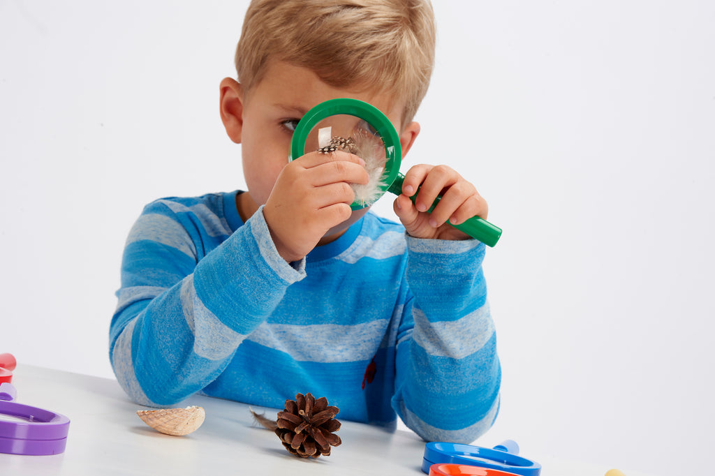 Young child looking through a green magnifying glass while holding small objects