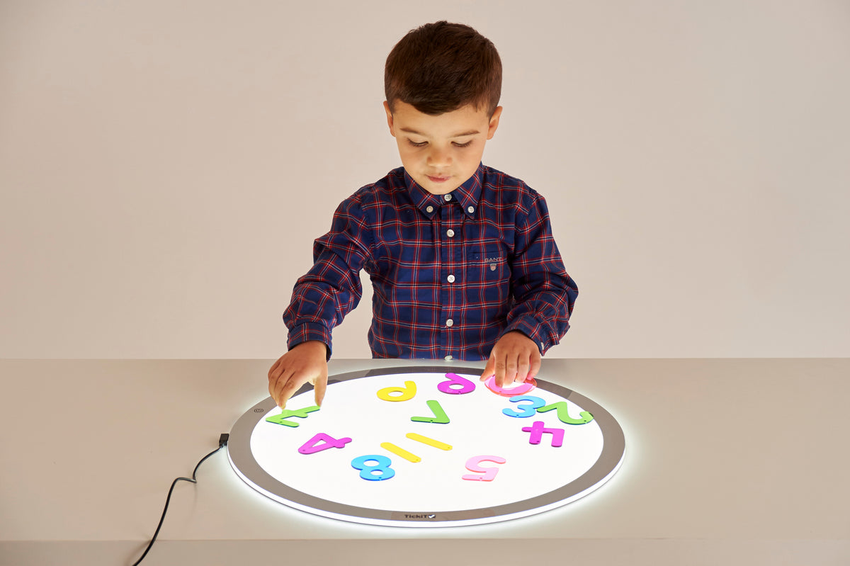 Child pressing colorful number tiles onto a round illuminated learning board