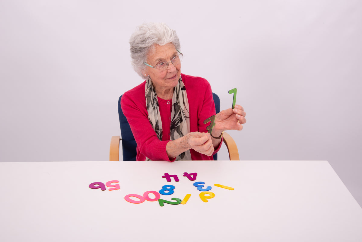 Older adult arranging colorful number tiles on a table in front of a seated chair