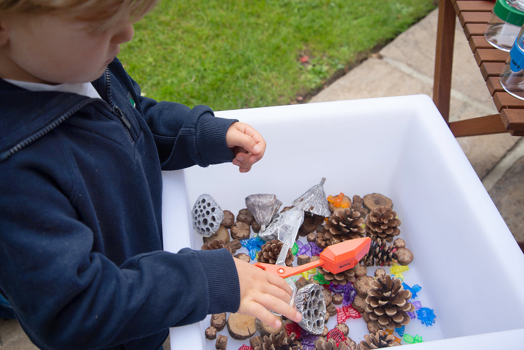 Child using colorful plastic tongs to pick up craft items in a bin