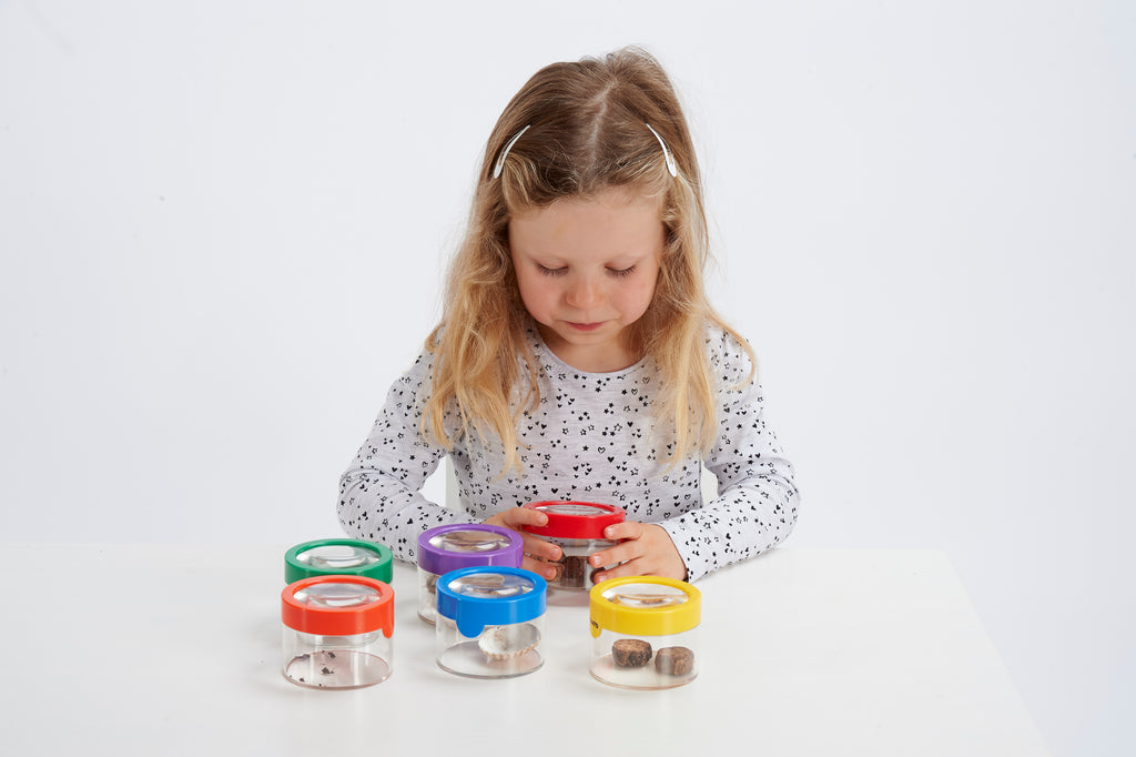Child examining clear viewer magnifiers with colorful lids and visible insects.