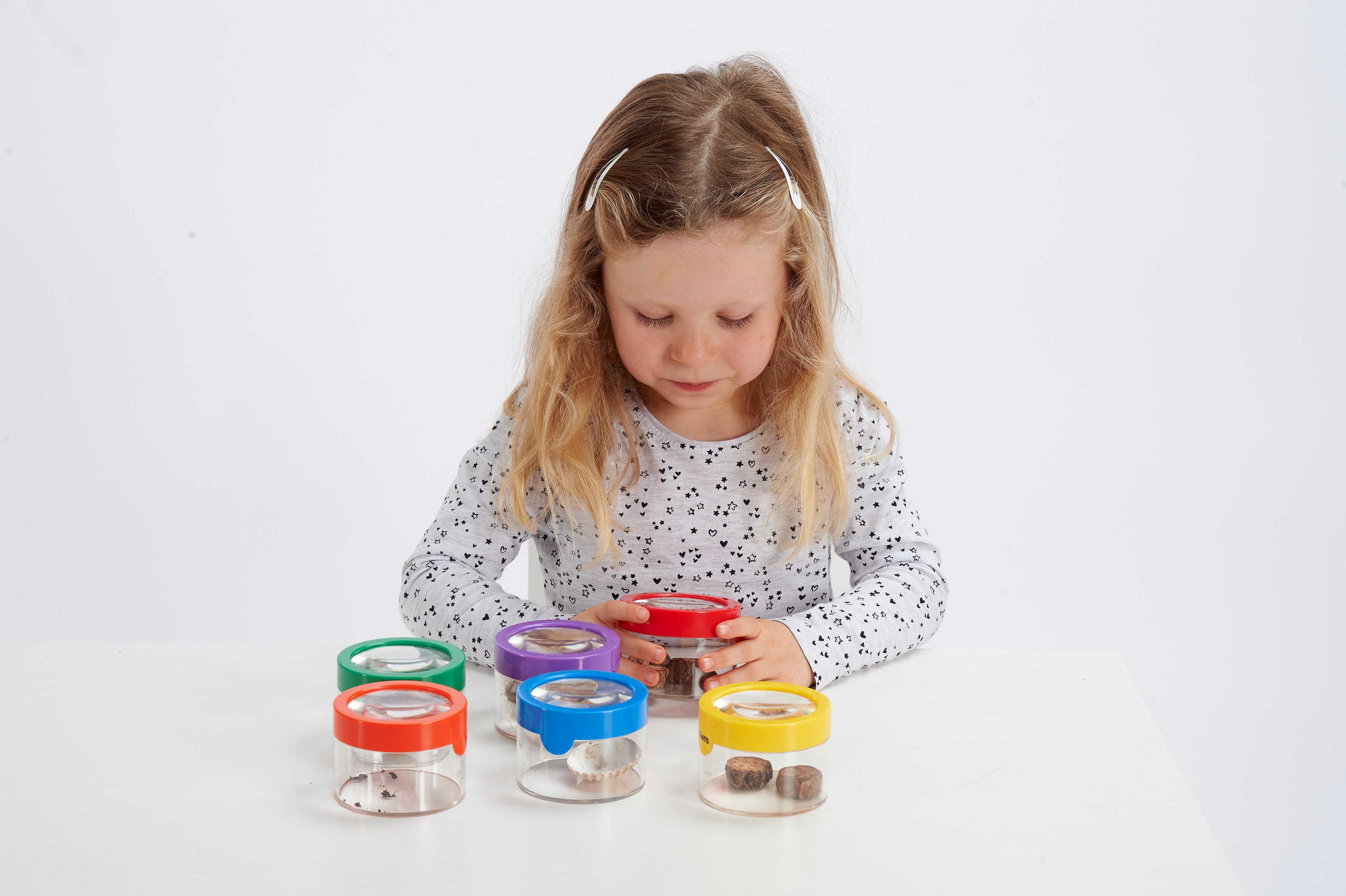 Child examining clear viewer magnifiers with colorful lids and visible insects.