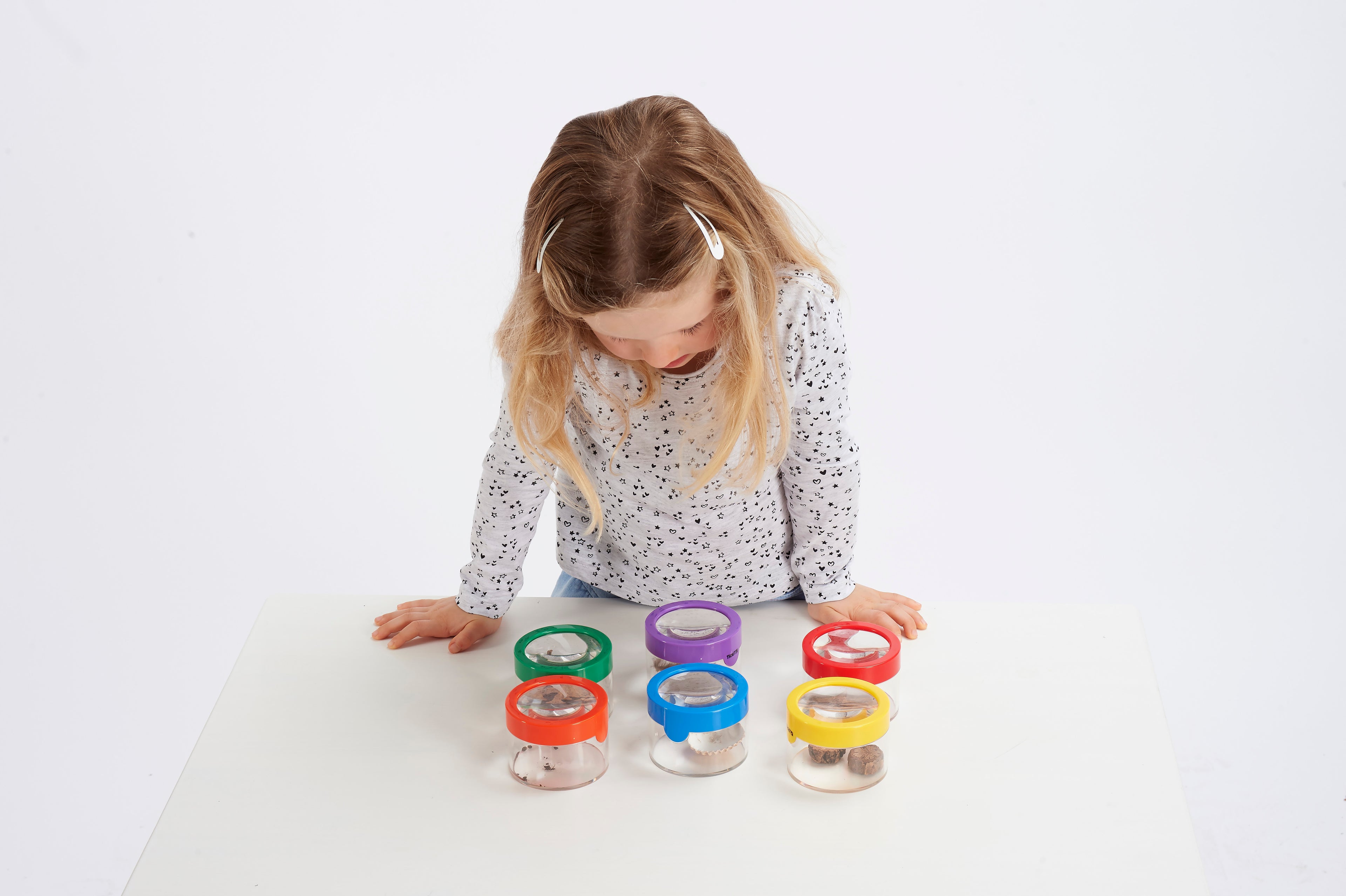 Child playing with multiple clear viewer magnifiers in colored containers on a table.