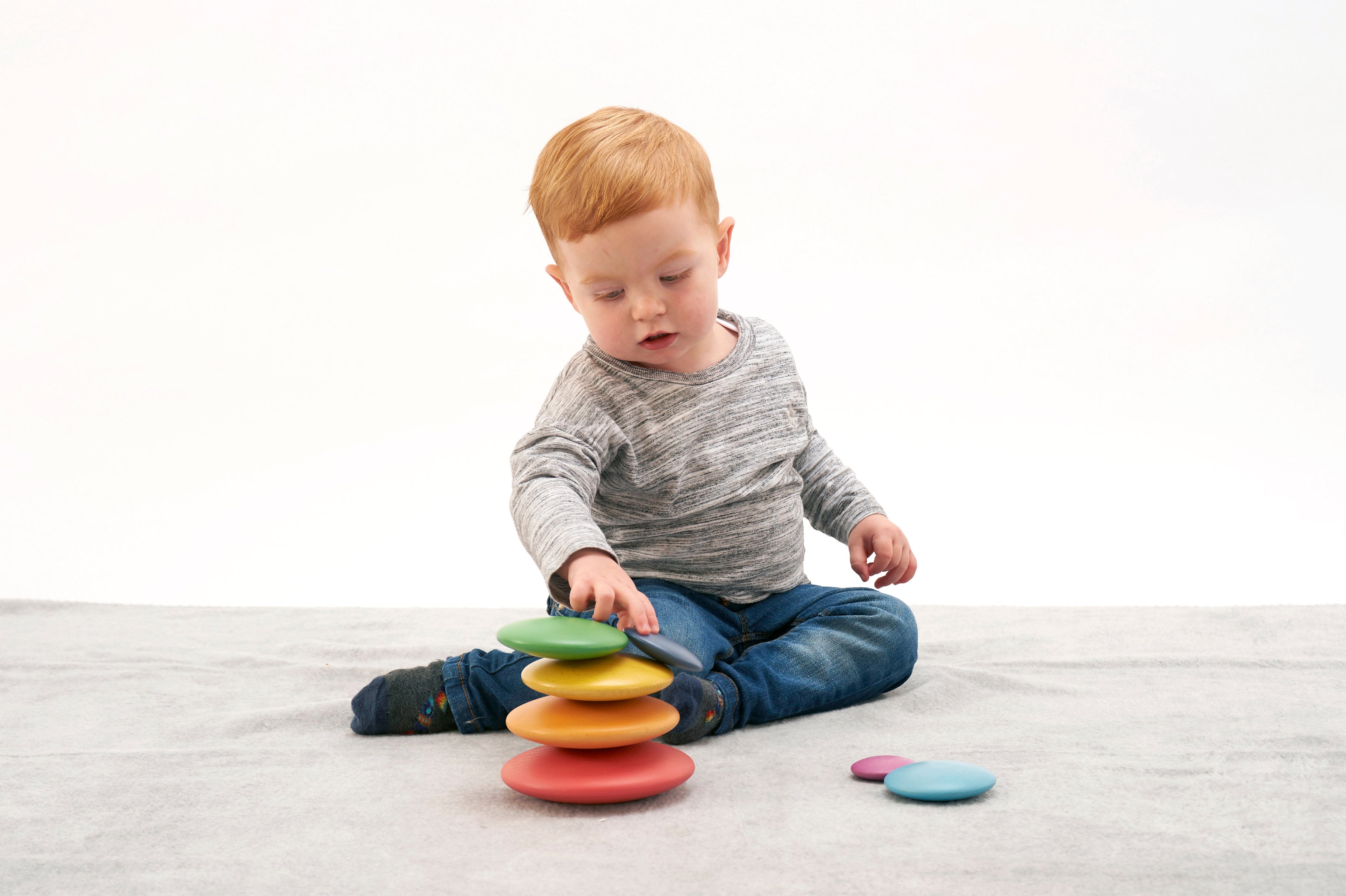 Seven rainbow wooden button disks stacked in a tower with scattered loose disks.