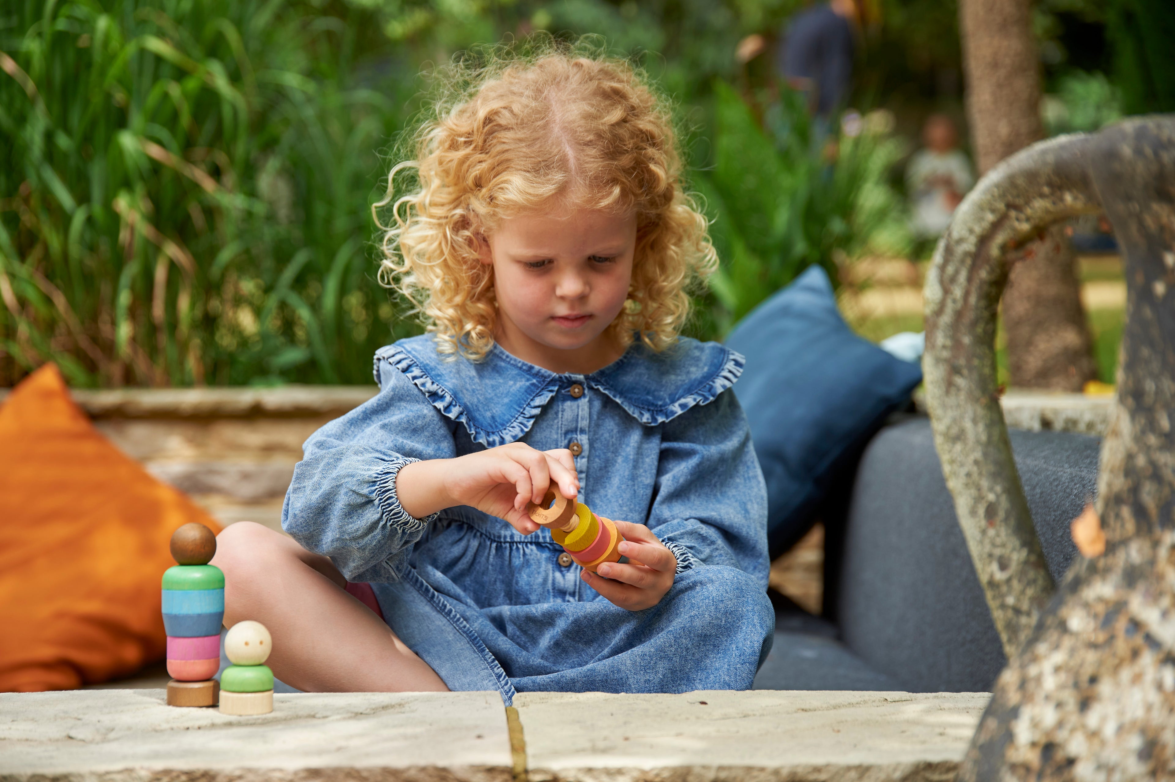 Child playing with a wooden rainbow peg people toy set on a bench