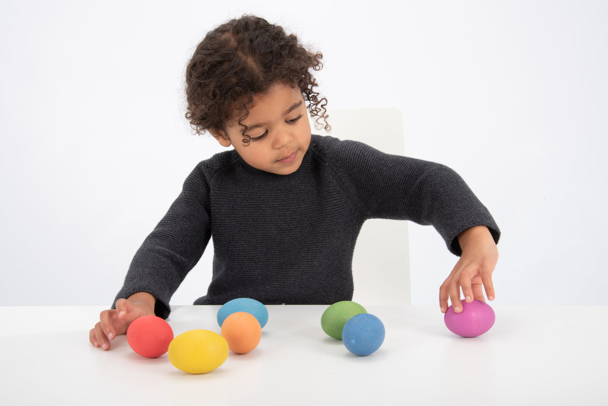 Child placing a pink multicolor wooden egg among pastel eggs