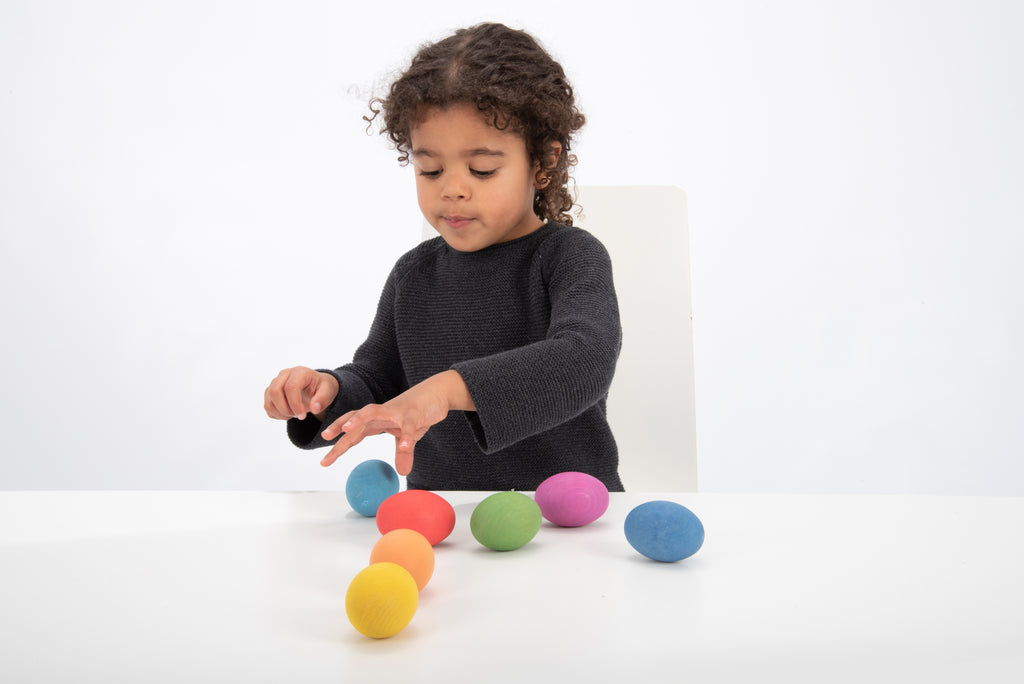 Child playing with multicolor wooden eggs on a table