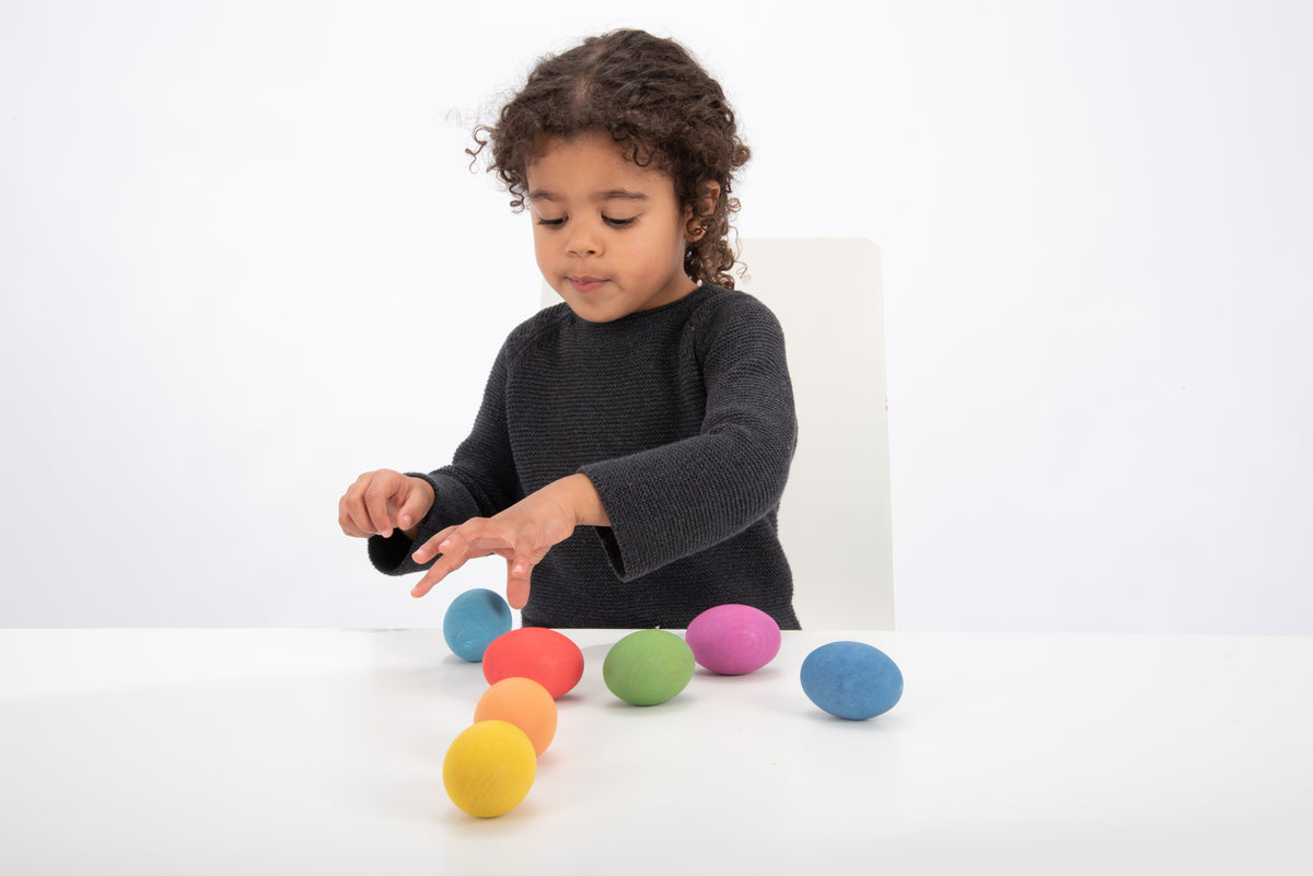 Child playing with multicolor wooden eggs on a table