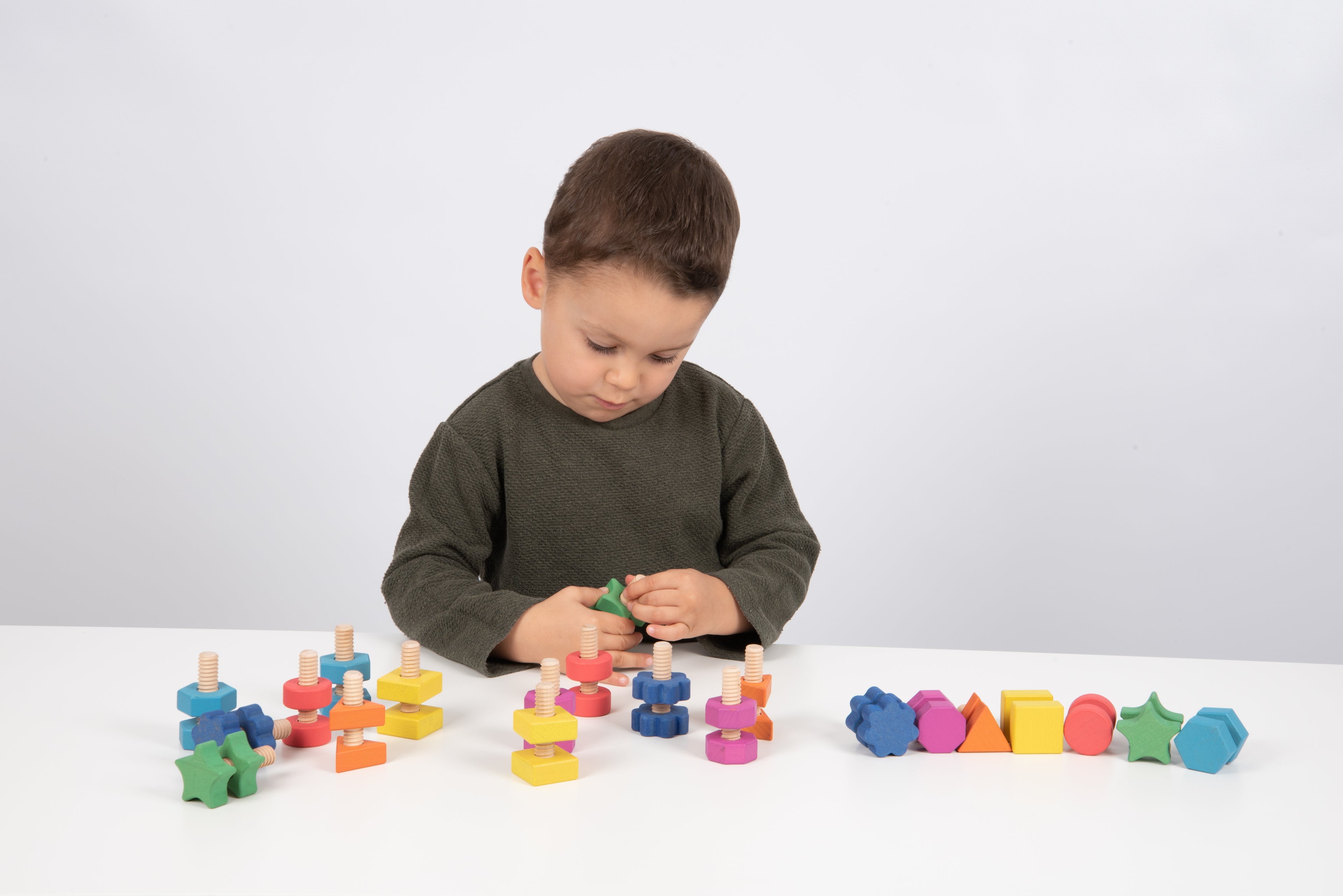 Child playing with rainbow wooden nut-and-bolt building pieces on a table