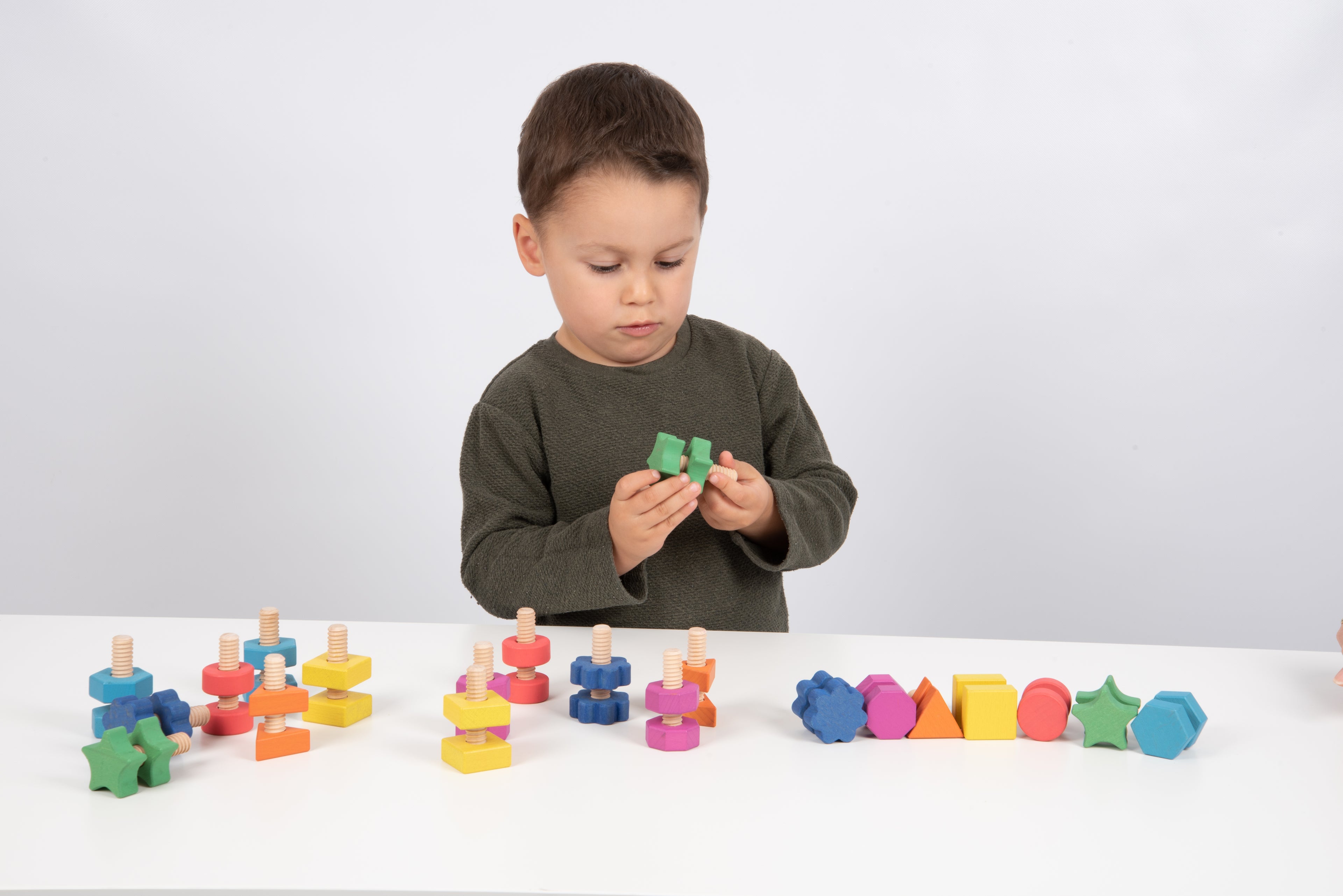 Child holding a green wooden nut-and-bolt building piece while playing