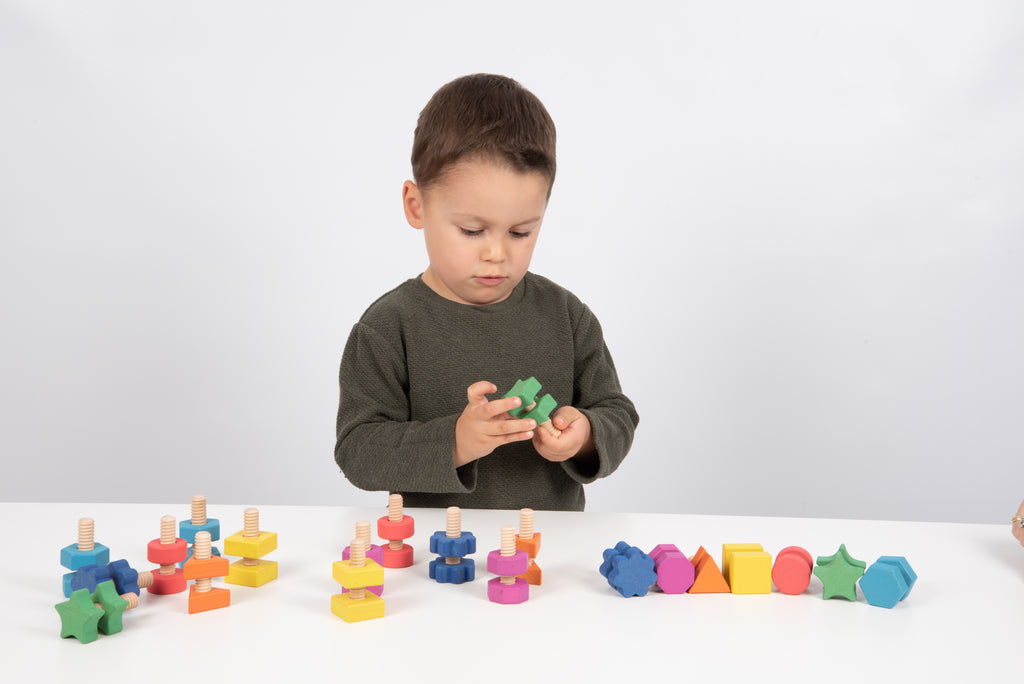 Child building with rainbow wooden nut-and-bolt pieces, colorful pieces on table